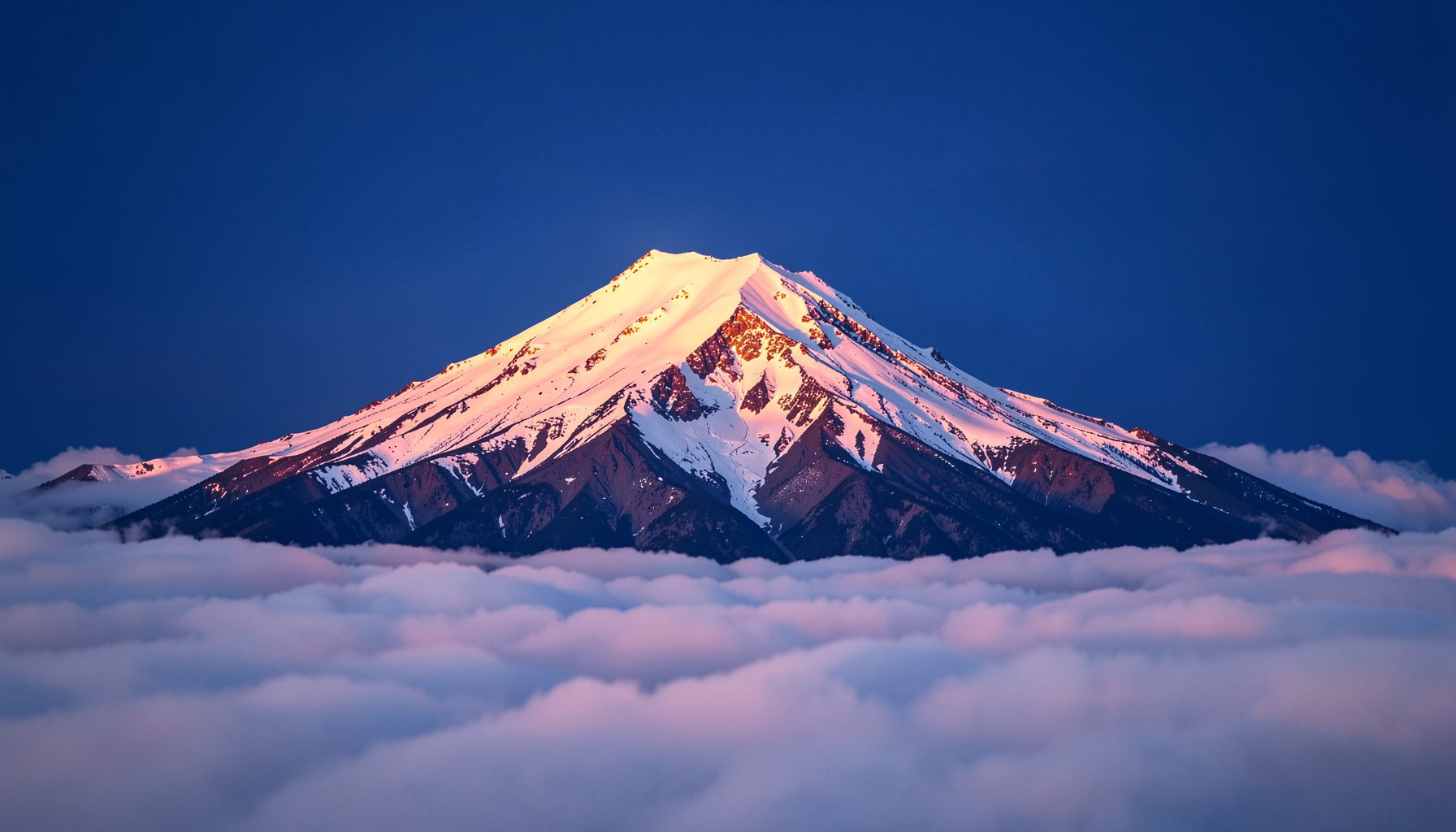 Snow-capped Mount Rainier rising above a sea of clouds at sunrise, pink and gold light on the summit