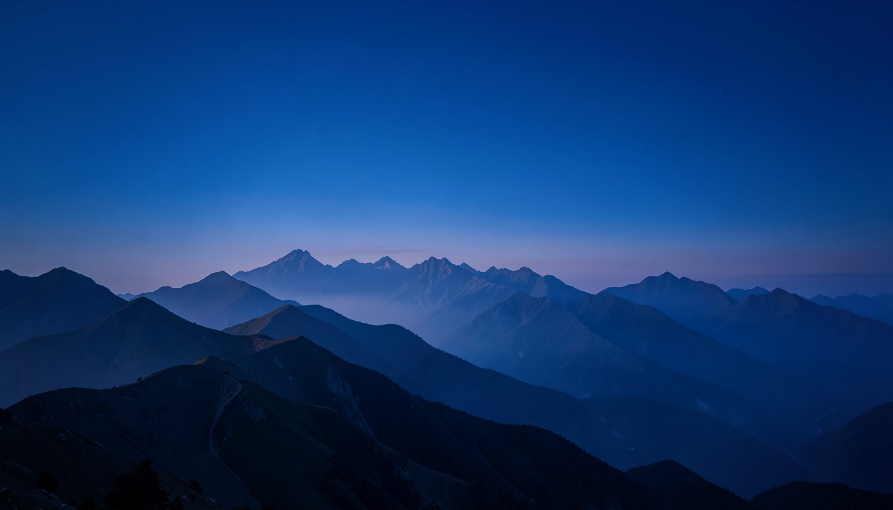Mountain ridgeline at dusk with layered peaks fading into mist, cool blue and soft lavender tones, serene and cinematic mood