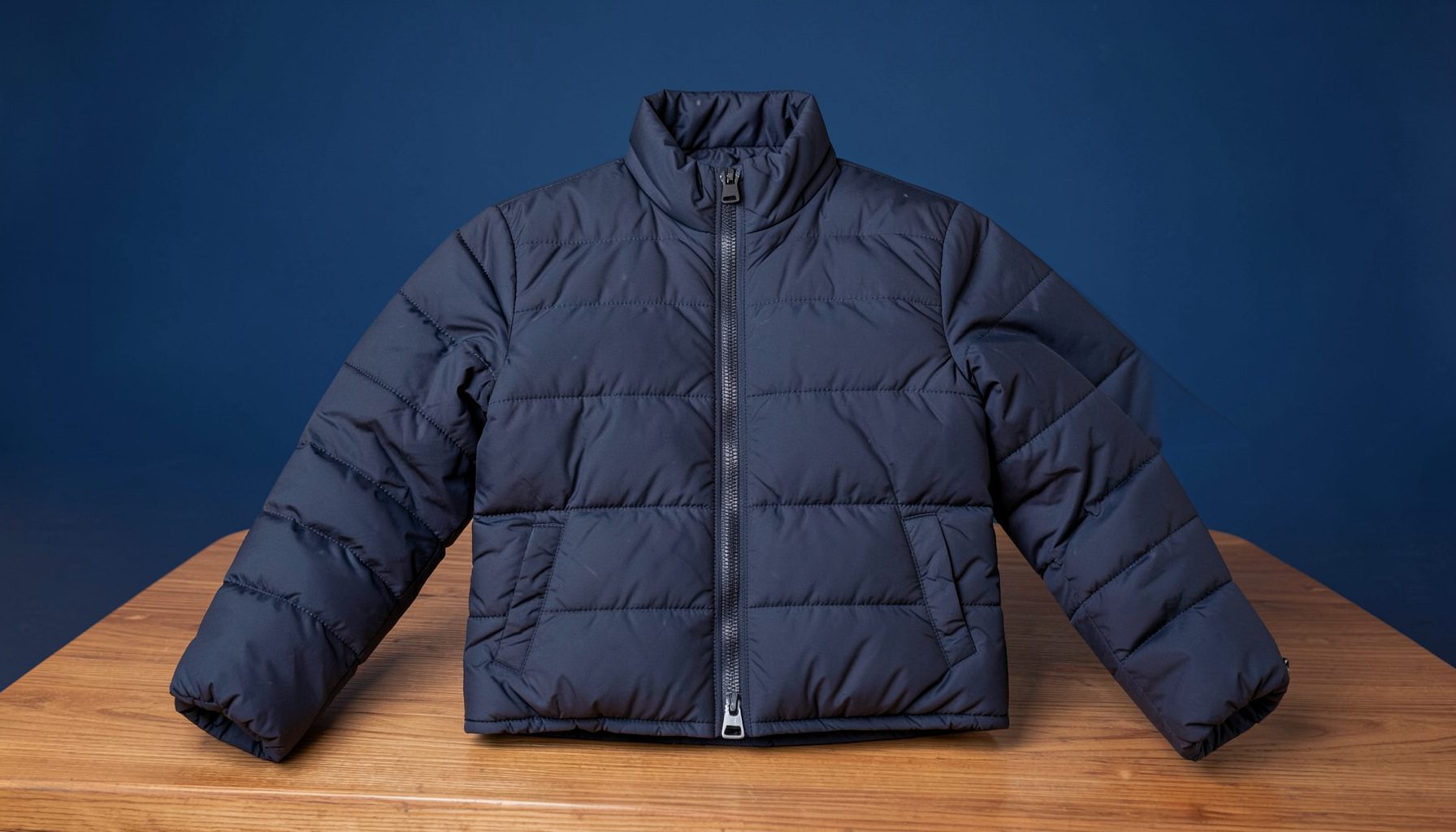 A navy blue insulated jacket with quilted baffles laid out on a wooden surface, crisp studio lighting, neutral backdrop