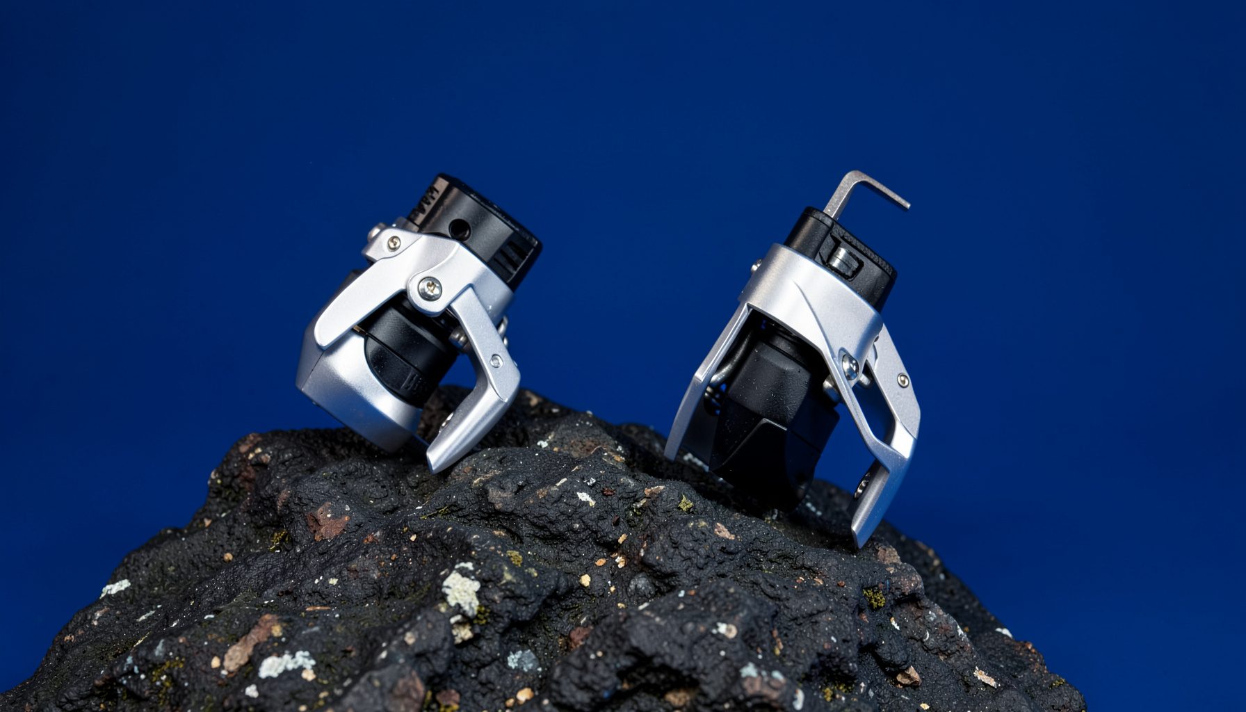 A pair of silver and black steel crampons with horizontal front points resting on dark rock, mountain gear aesthetic
