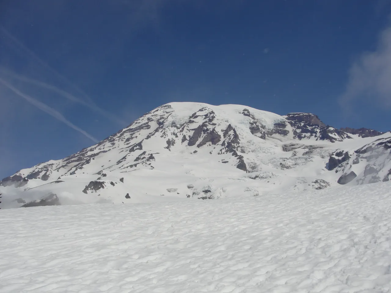 Snow-capped mountain peak under clear blue sky with faint jet contrails, bright and crisp mood